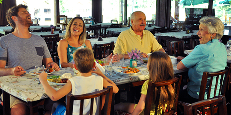 Família alegre reunida em mesa de refeição do hotel fazenda perto de SP