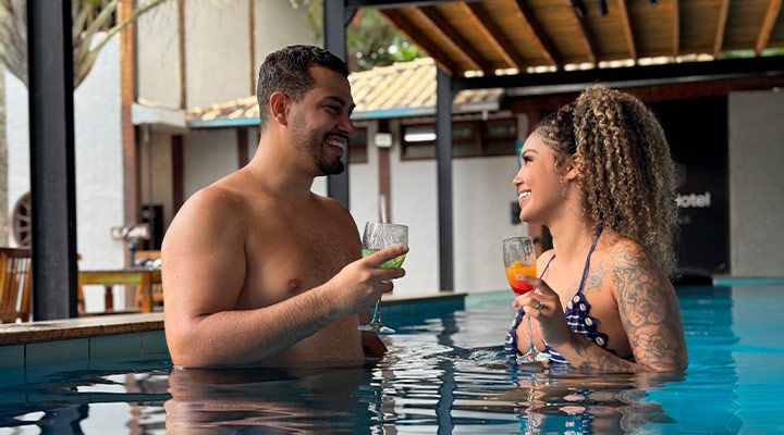 Casal se divertindo na piscina, brindando com drinks coloridos em clima descontraído. Perfeito para momentos românticos.