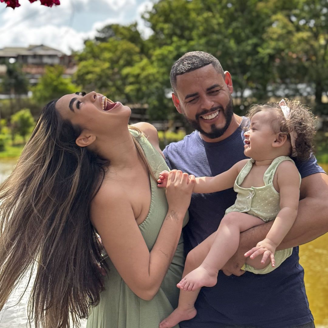 Pais com a filha sorrindo em frente a um lago ao ar livre