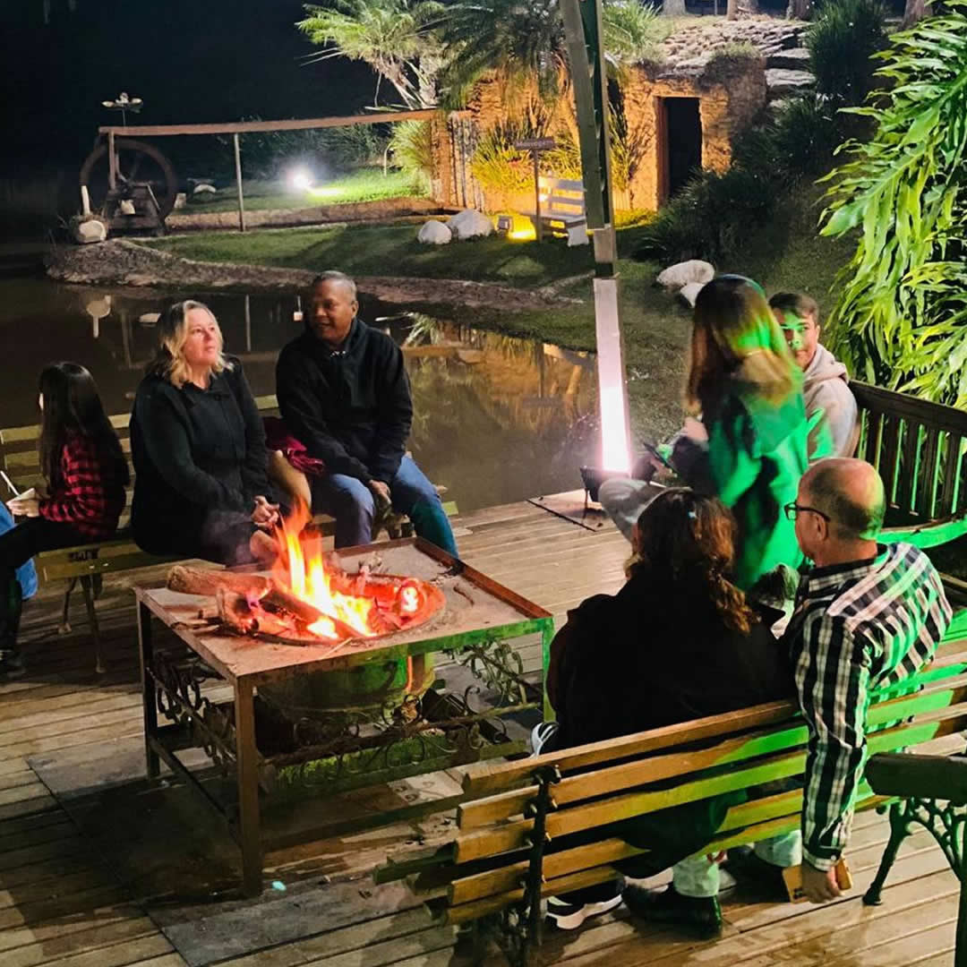 Família e amigos reunidos em volta de uma fogueira ao ar livre, aproveitando momento de confraternização