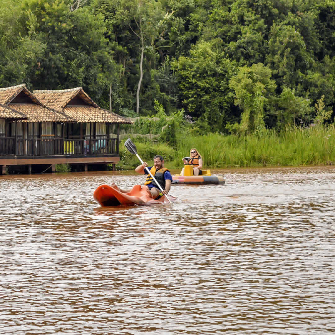 Casal remando de caiaque em um lago tranquilo cercado pela natureza.