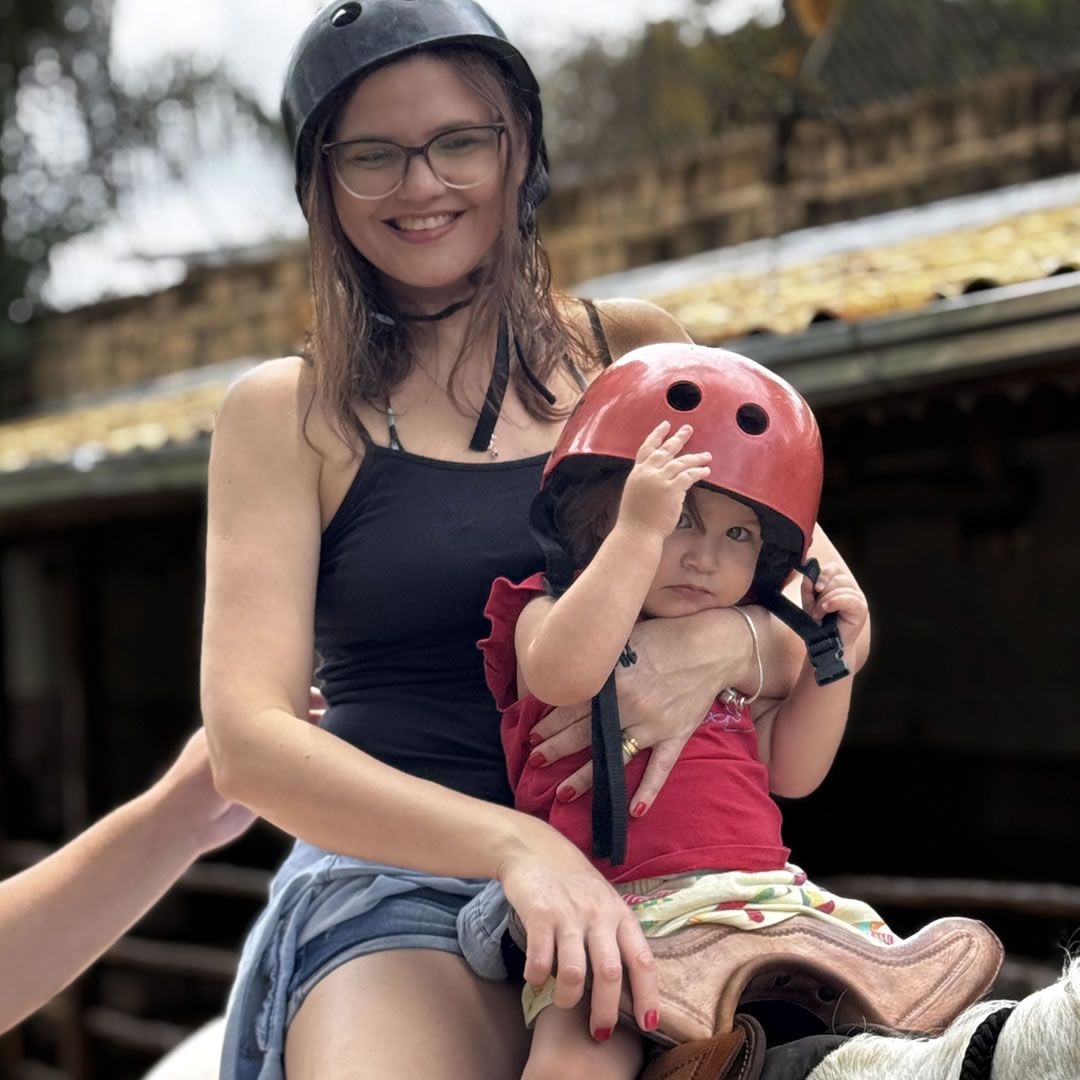 Mãe e filha andando a cavalo juntas em um ambiente ao ar livre.