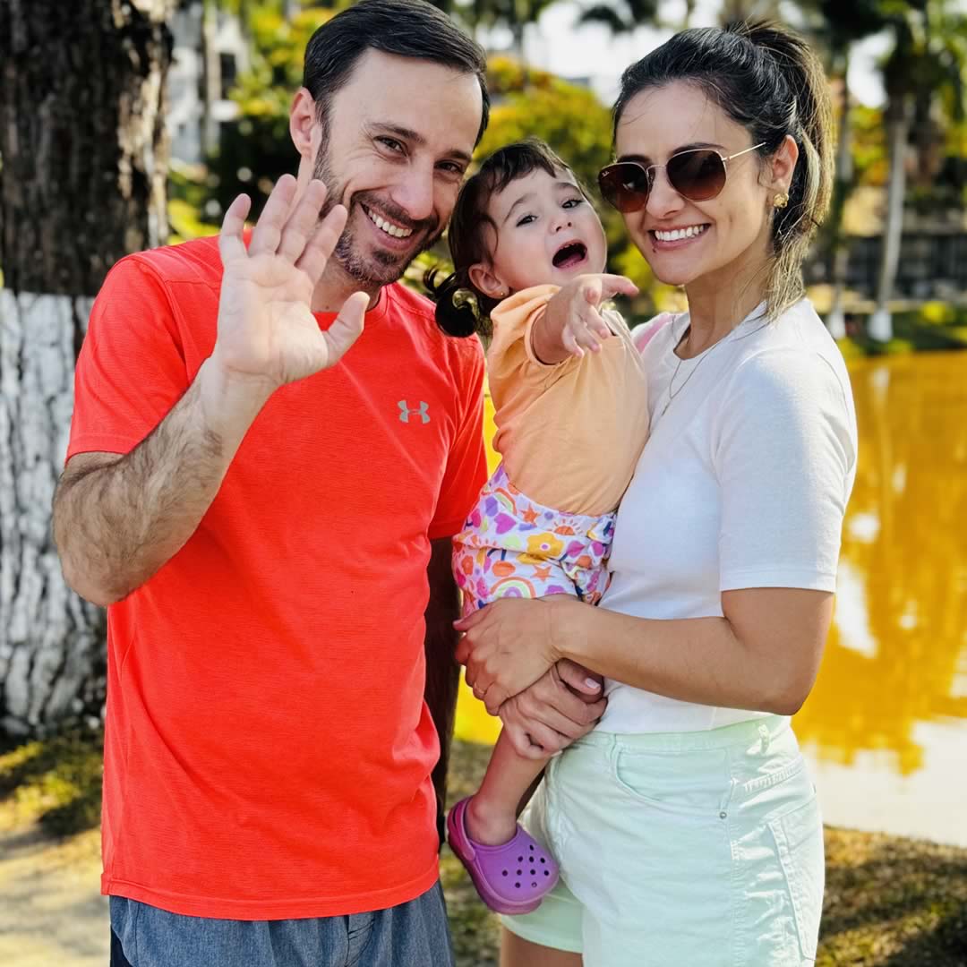 Família feliz sorrindo em frente a um lago ao ar livre.