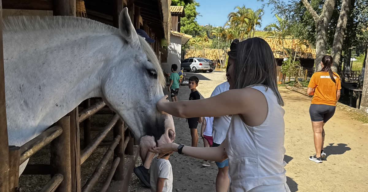hospede fazendo carinho em um cavalo na fazendinha do Park Hotel Modelo
