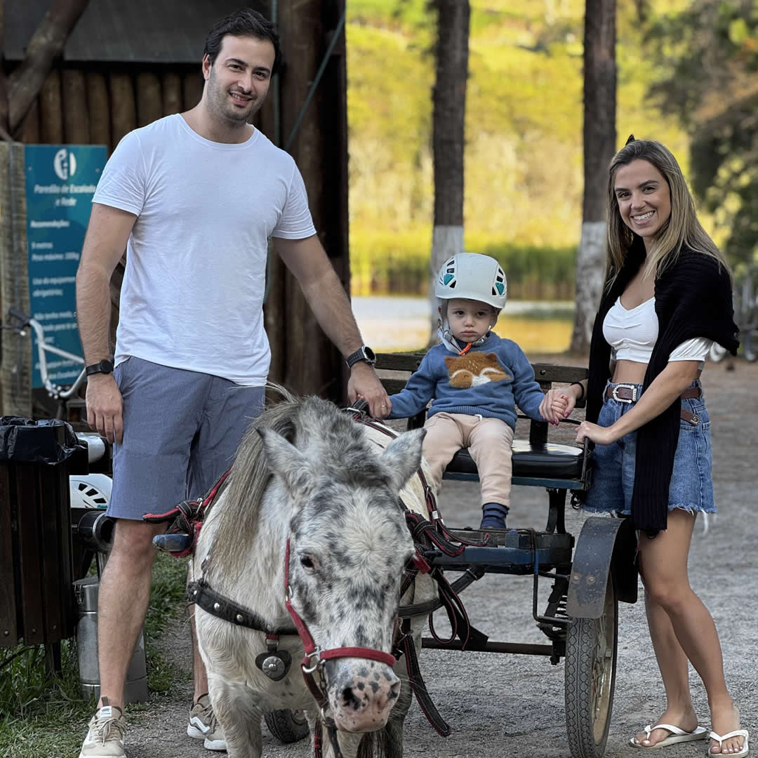Familia sorrindo para foto com uma criança dentro de uma carroça sendo puxada por um ponei