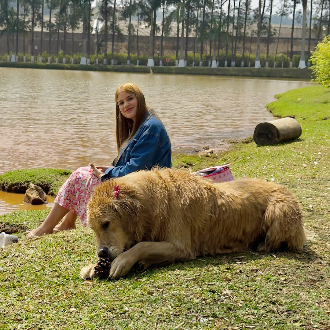 Hospede com cachorro sentados em frente ao lago em hotel fazenda