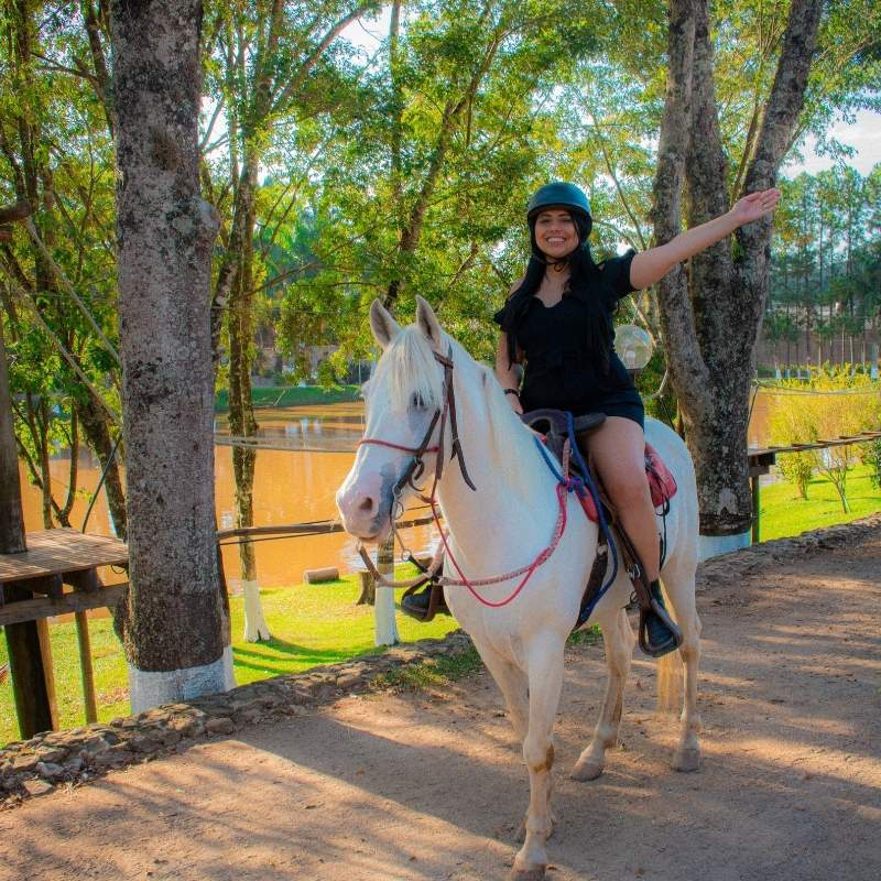 Mulher sorridente passeando de cavalo em parque com árvores verdes ao fundo, cenário ao ar livre perfeito para passeios de equitação